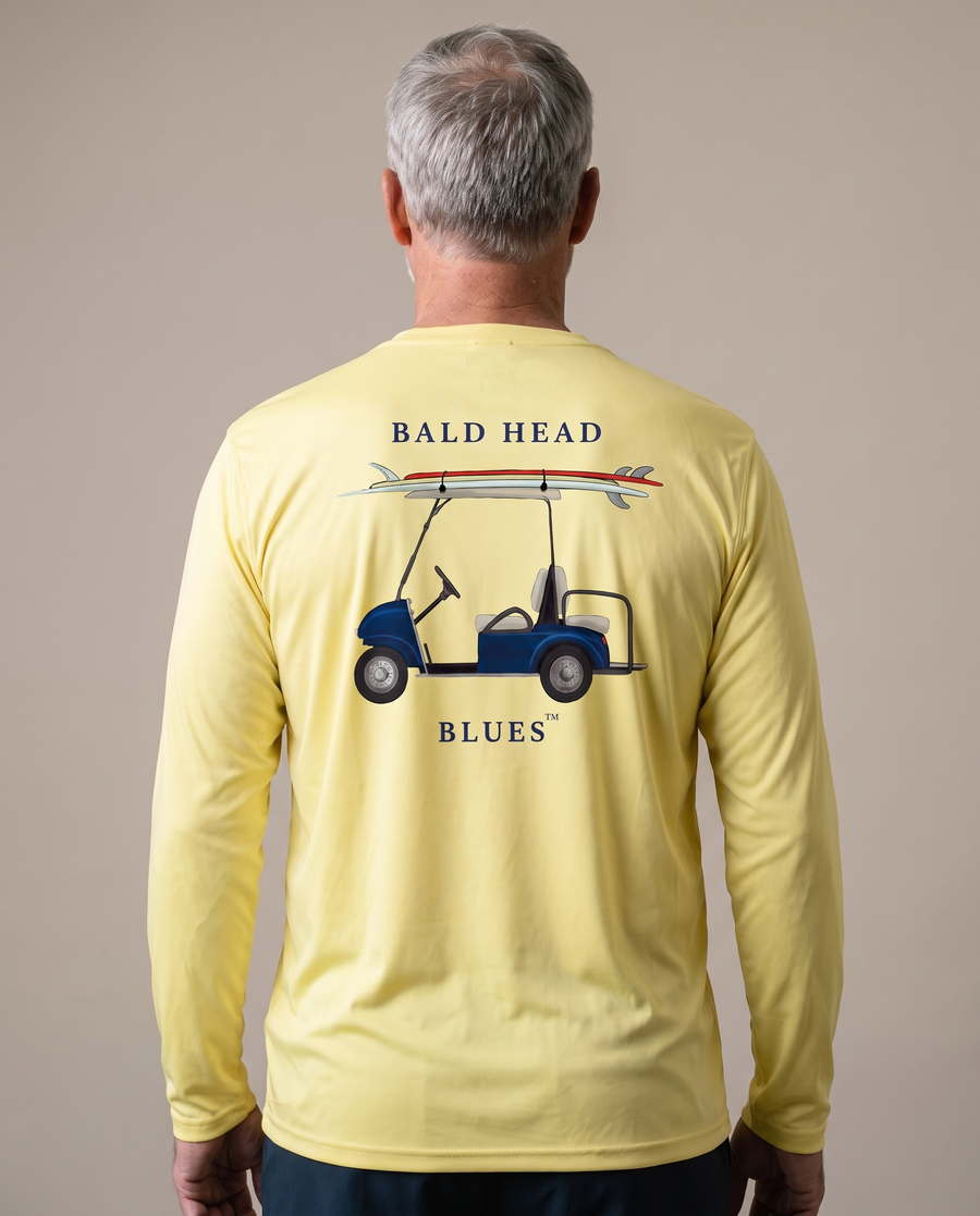 Studio back view of a man wearing the Performance Long Sleeve Golf Cart T-Shirt in Pale Yellow with the Bald Head Blues cart and surfboard print