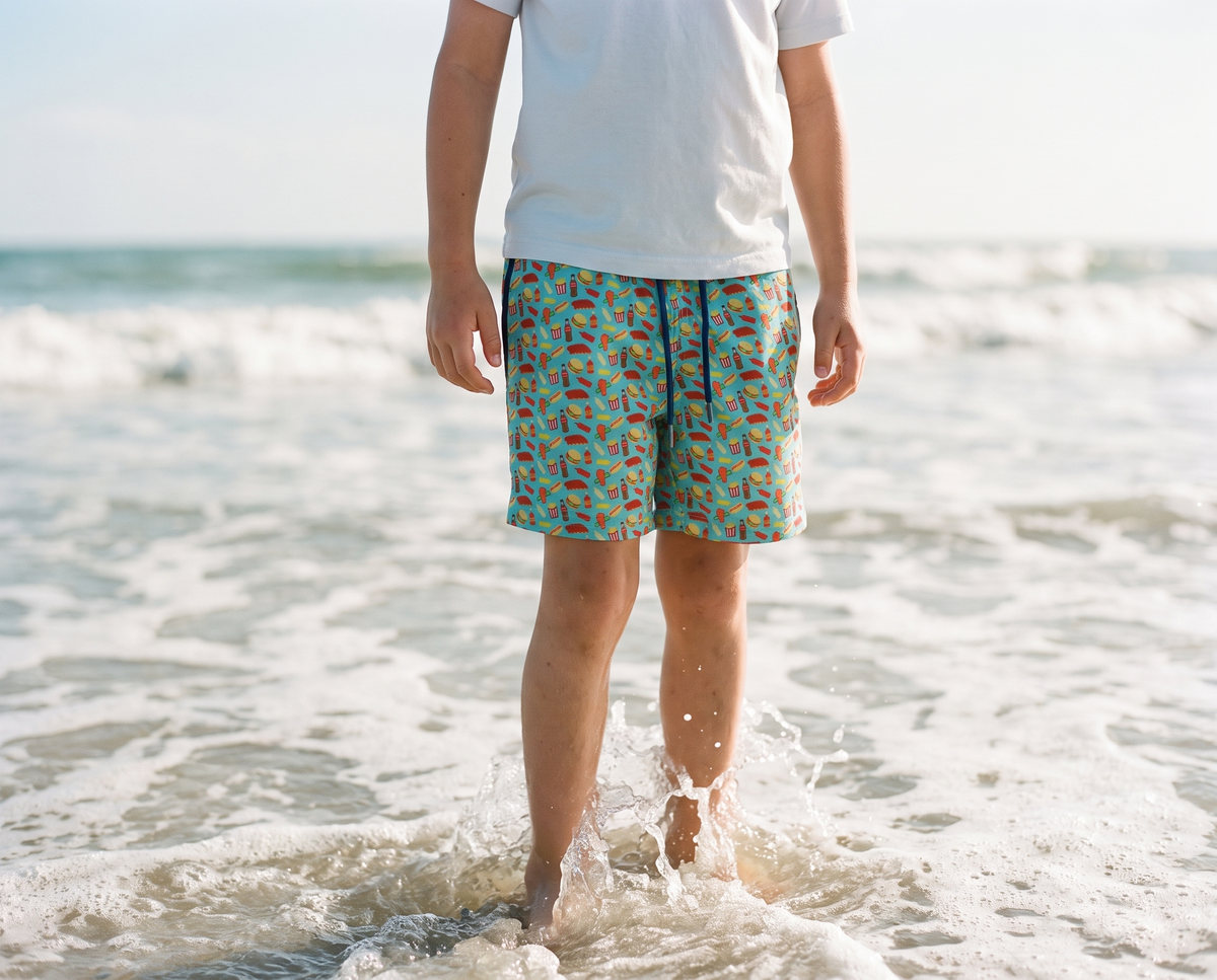 Boy in the shallow surf wearing Bald Head Blues youth Aruba cookout print swim trunks